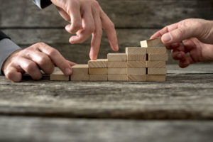 team effort on the way to success - two male hands building stable steps with wooden pegs for the third one to walk his fingers up towards personal and career growth. - ID 48425775